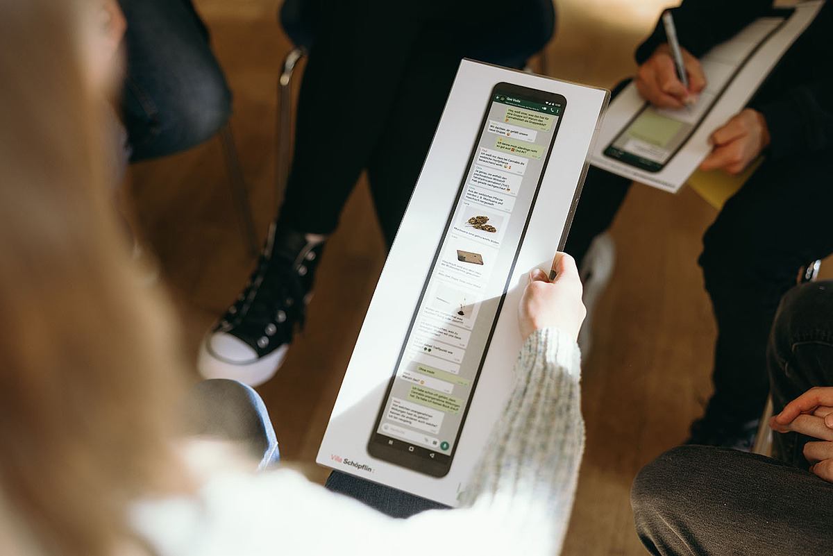 Eine Person hält ein Bild, auf dem ein Smartphone mit einem langen Chatverlauf zu sehen ist. 