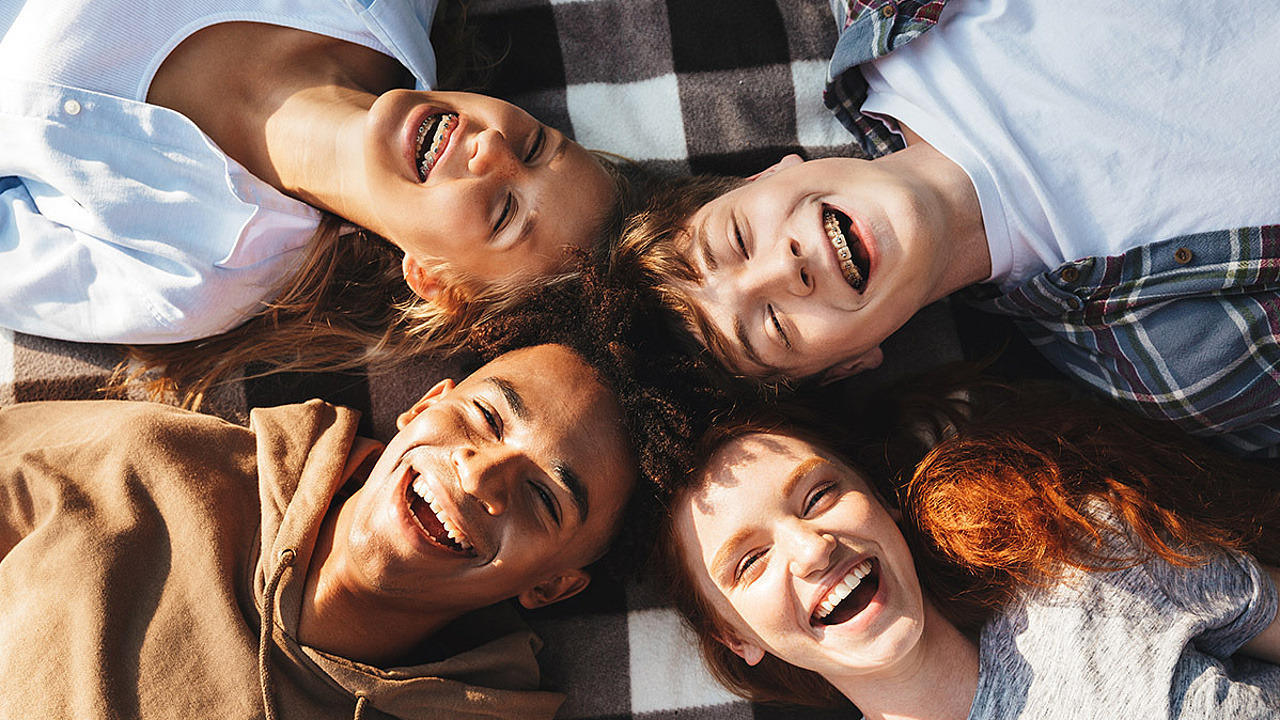 Porträt von glücklichen Jungen und Mädchen, die lachen und draußen auf einer Decke im Kreis liegen.