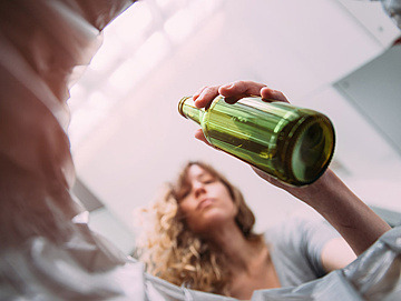 Eine Frau wirft eine Flasche in einen Mülleimer